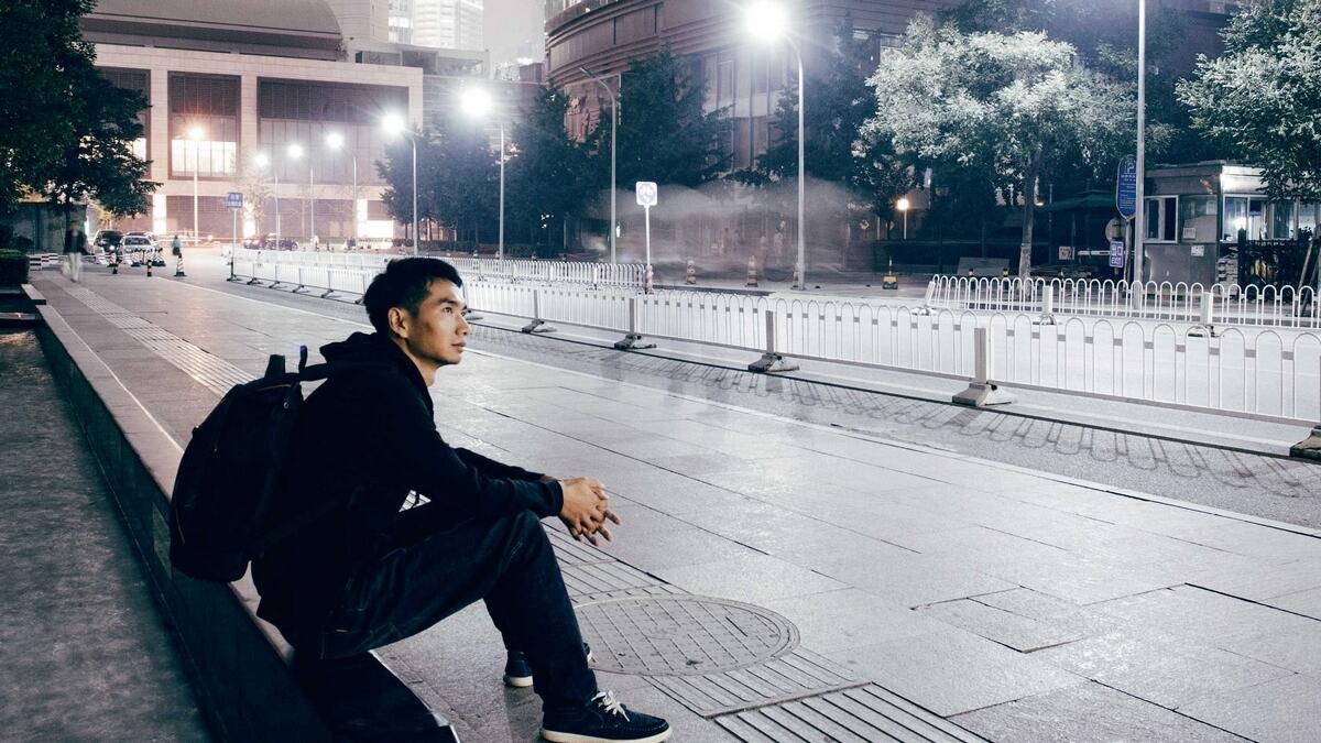 a man sitting on a bench in a city at night with a backpack on his back and a backpack on his shoulder