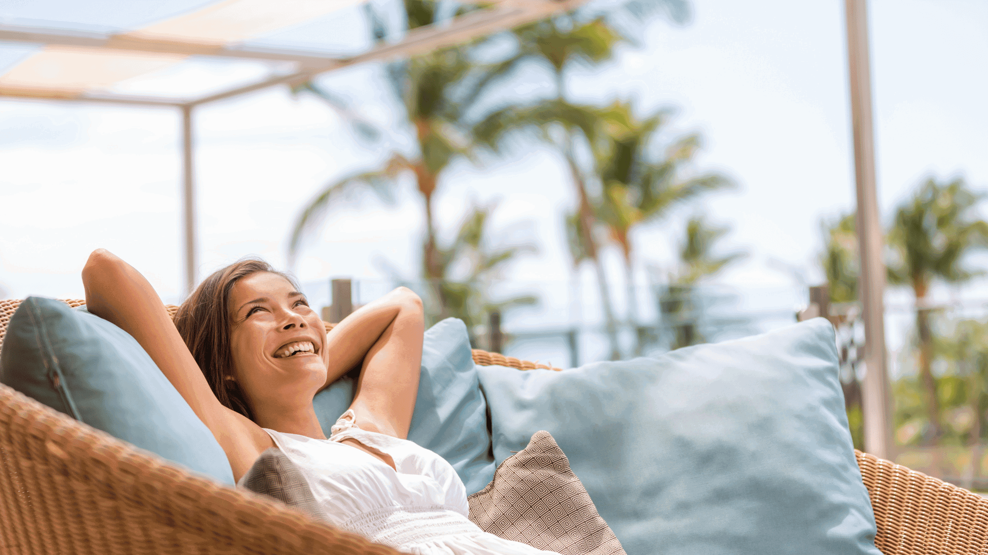 a woman laying in a wicker chair with a blue pillow on it and smiling at the camera