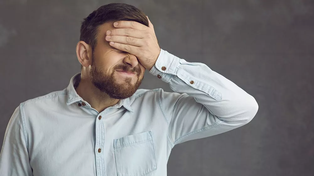 a man holding his head with his hands while looking at something with a surprised look on his face and hands on his forehead