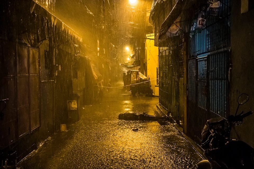 a dark alley with a motorcycle parked on the side of it and a light shining down on the street